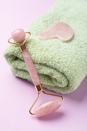 Photo of Natural face roller, towel and gua sha tool on pink background