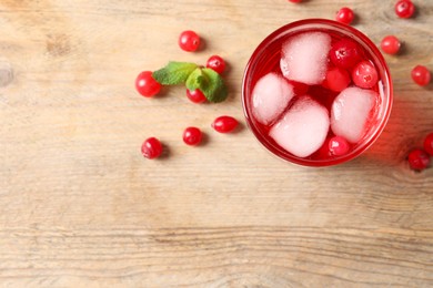 Photo of Tasty cranberry juice with ice cubes in glass and fresh berries on wooden table, top view. Space for text