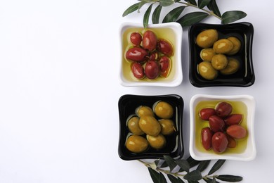 Bowls with different ripe olives and leaves on white background, flat lay. Space for text