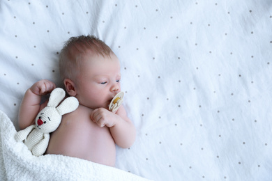 Photo of Cute newborn baby with toy lying in bed, top view. Space for text