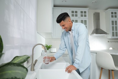 Man filling glass with water from tap in kitchen