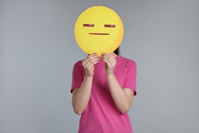 Photo of Woman holding emoticon with closed eyes and mouth on grey background