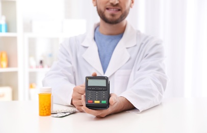 Photo of Pharmacist with payment terminal and pills in drug store, closeup
