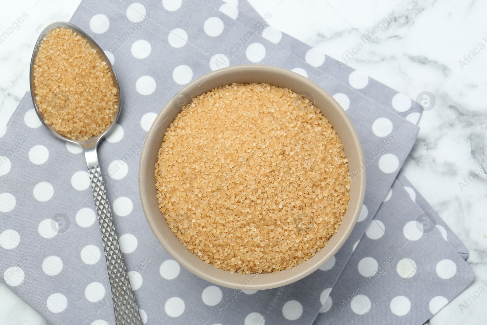 Photo of Brown sugar in bowl and spoon on white marble table, top view