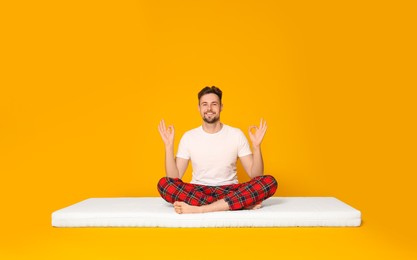 Man sitting on soft mattress and meditating against orange background