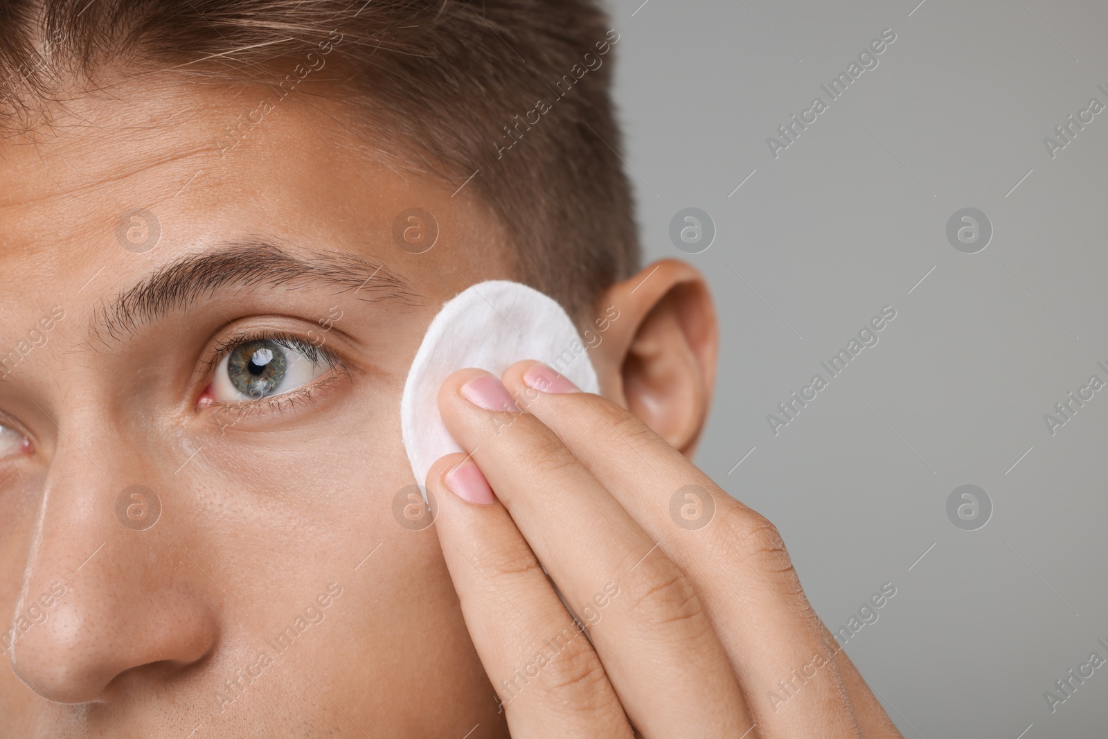 Photo of Man cleaning face with cotton pad on grey background, closeup