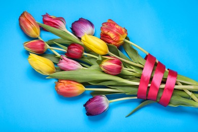 Photo of Bouquet of beautiful colorful tulip flowers tied with red ribbon on light blue background, top view