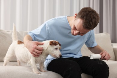 Photo of Pet shedding. Man with lint roller removing dog's hair from pants on sofa at home