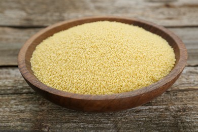 Photo of Bowl of raw couscous on wooden table, closeup