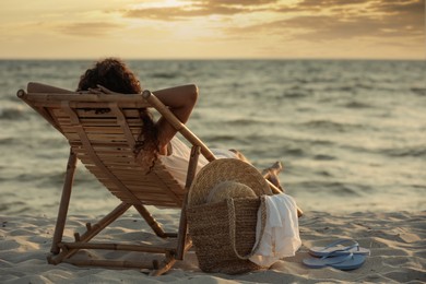 Woman resting in wooden sunbed on tropical beach at sunset