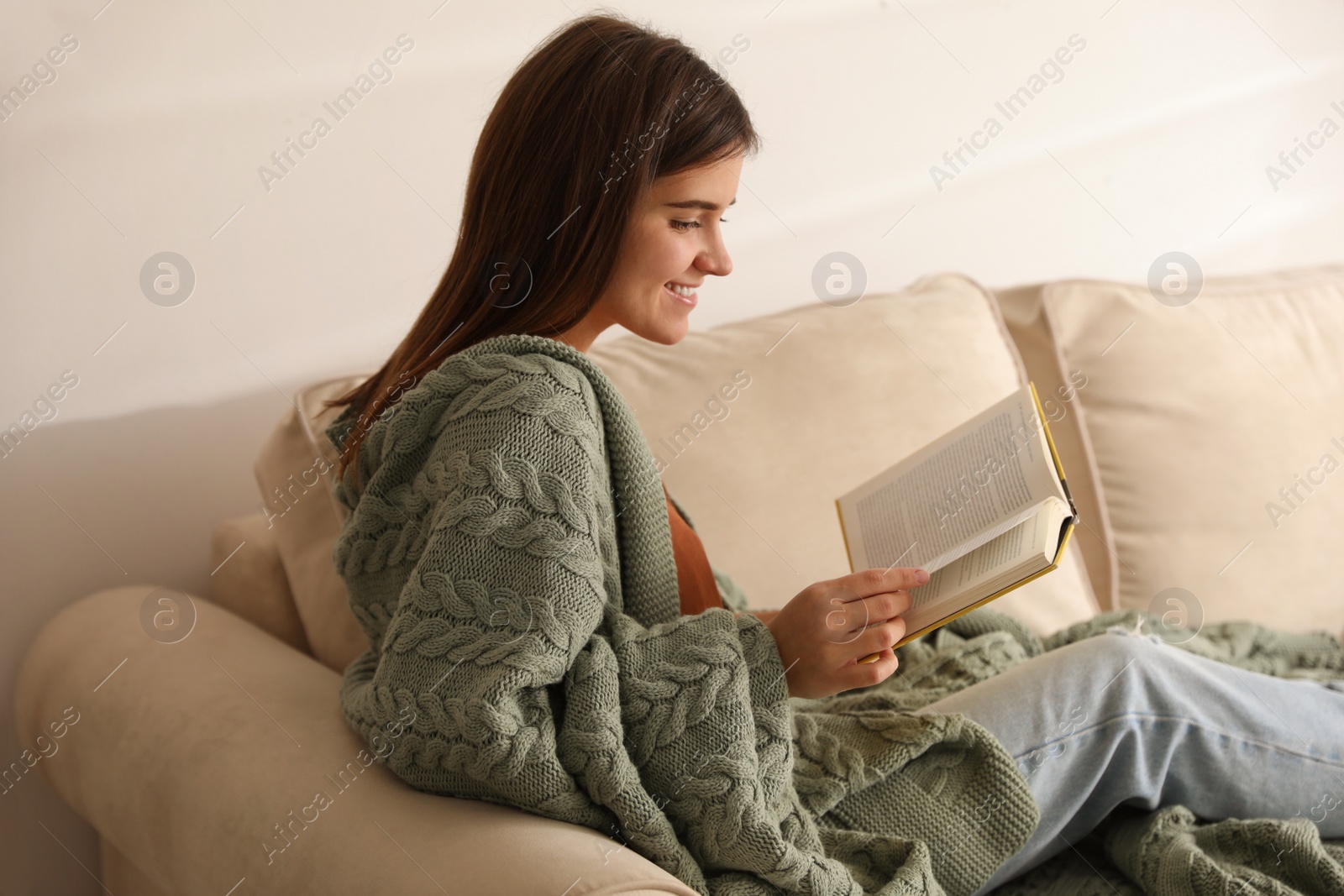 Photo of Woman covered with warm green plaid reading book on sofa at home