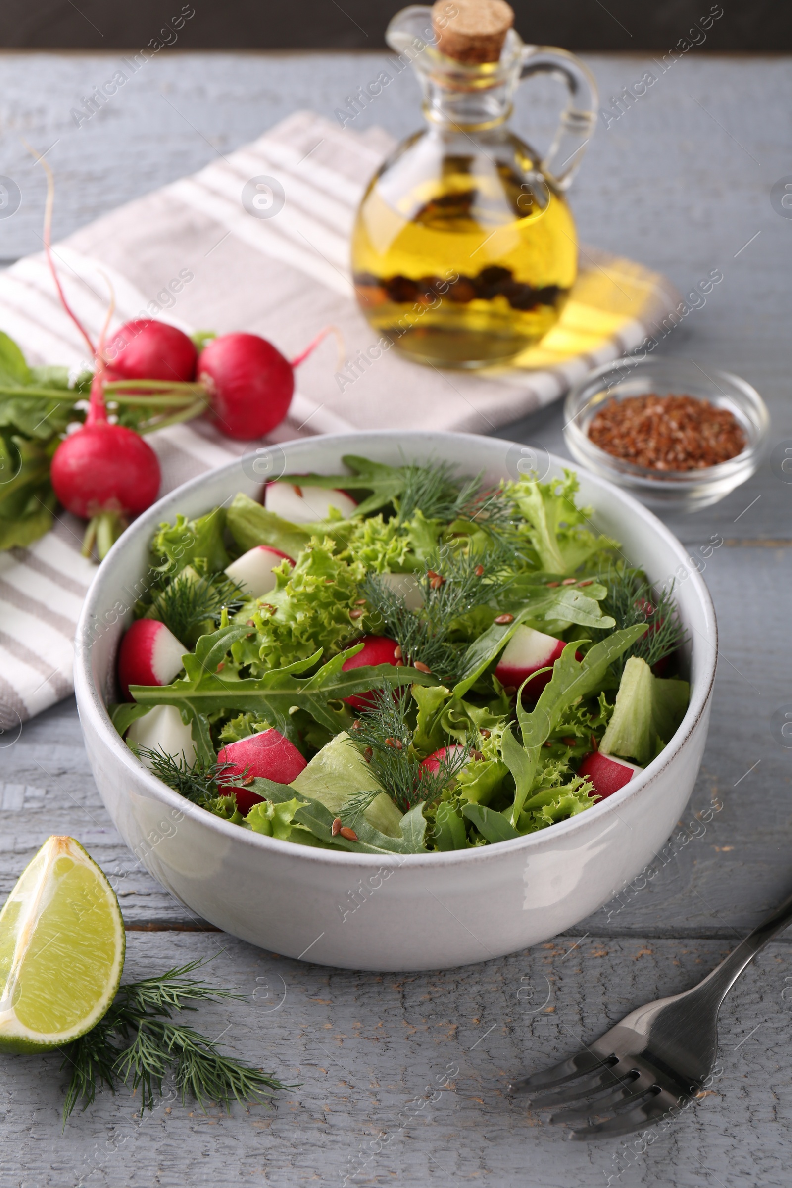 Photo of Delicious radish salad, ingredients and fork on light gray wooden table