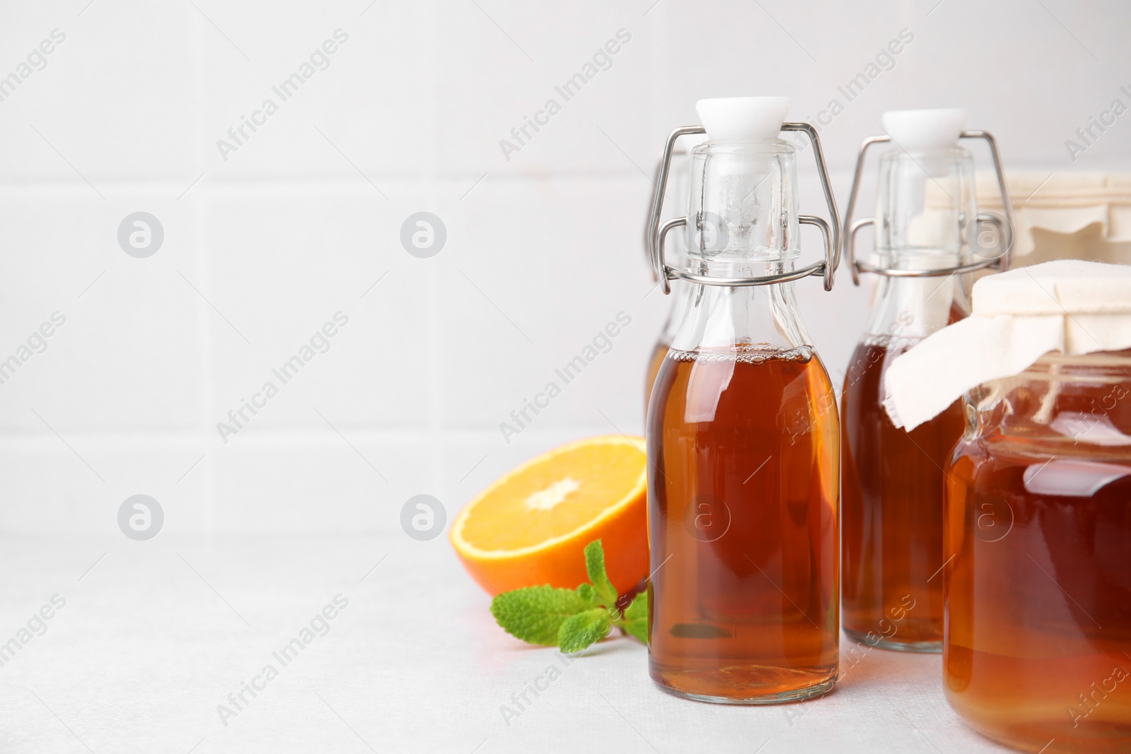 Photo of Tasty kombucha, orange and mint on white table, space for text