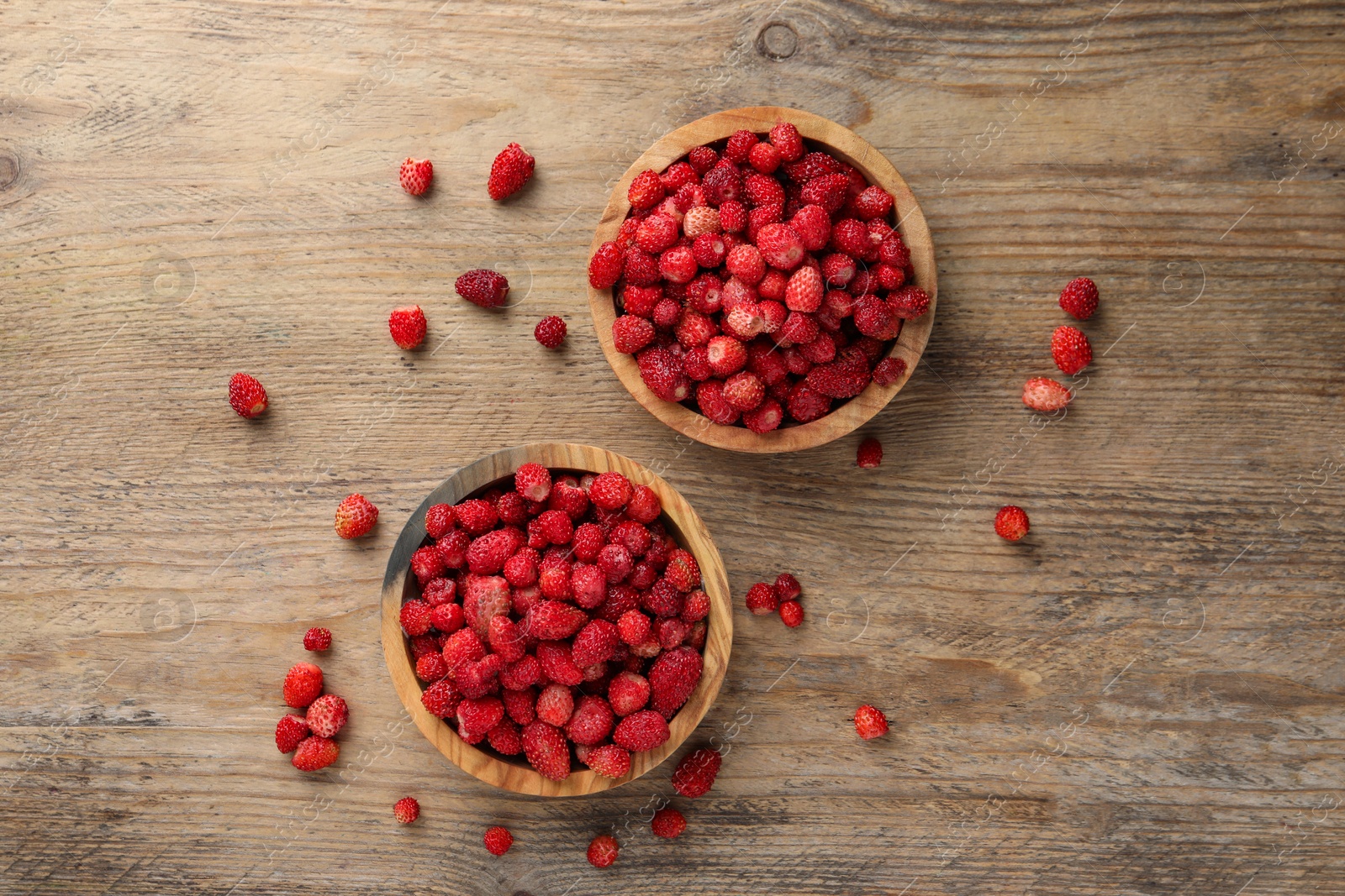 Photo of Fresh wild strawberries in bowls on wooden table, flat lay