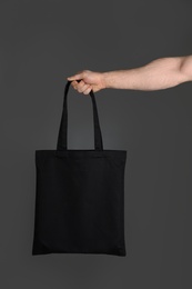 Man holding cotton shopping eco bag on grey background. Mockup for design