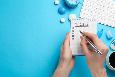 Photo of Woman filling To Do list in notepad at light blue table, closeup. Space for text