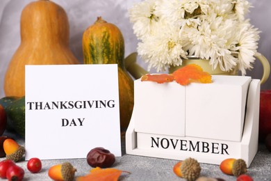 Photo of Thanksgiving day, holiday celebrated every fourth Thursday in November. Autumn composition with wooden block calendar and paper card on grey table