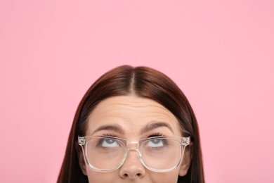 Photo of Woman in stylish eyeglasses looking up on pink background, closeup. Space for text