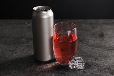 Energy drink in glass, aluminium can and ice cubes on grey table