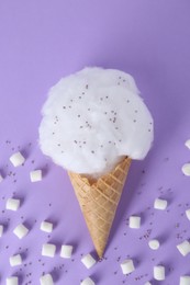 Photo of Sweet cotton candy in waffle cone and marshmallows on purple background, flat lay