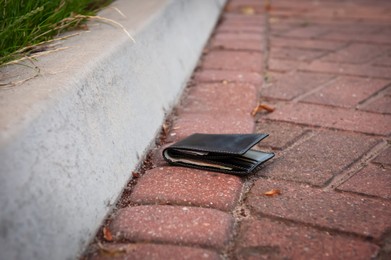 Black wallet on pavement outdoors. Lost and found