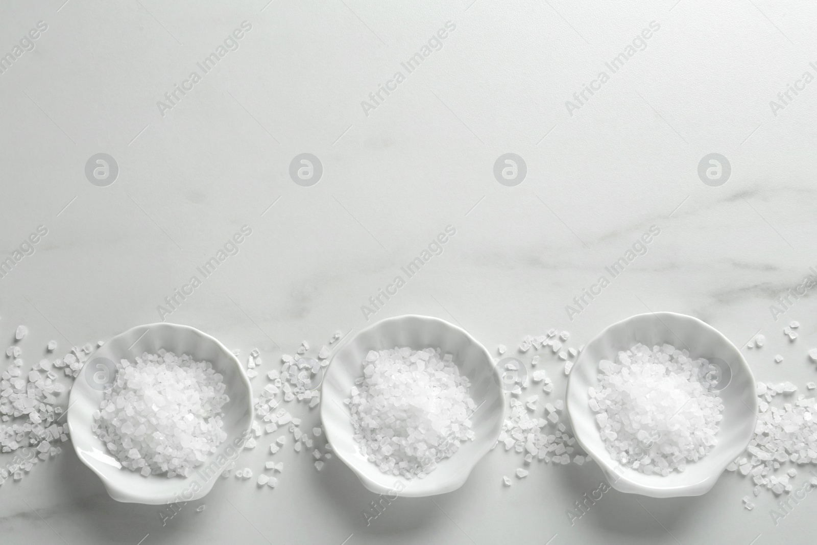 Photo of Natural sea salt on white marble table, flat lay. Space for text