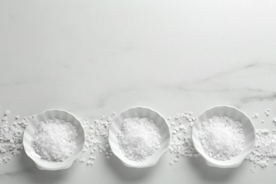 Natural sea salt on white marble table, flat lay. Space for text