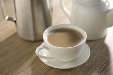 Photo of Aromatic tea with milk in cup, teapot and pitcher on wooden table, closeup