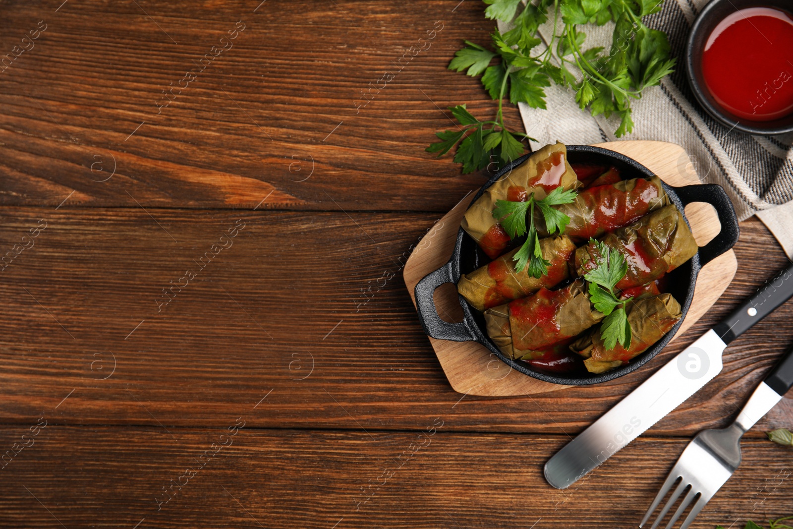 Photo of Delicious stuffed grape leaves with tomato sauce on wooden table, flat lay. Space for text