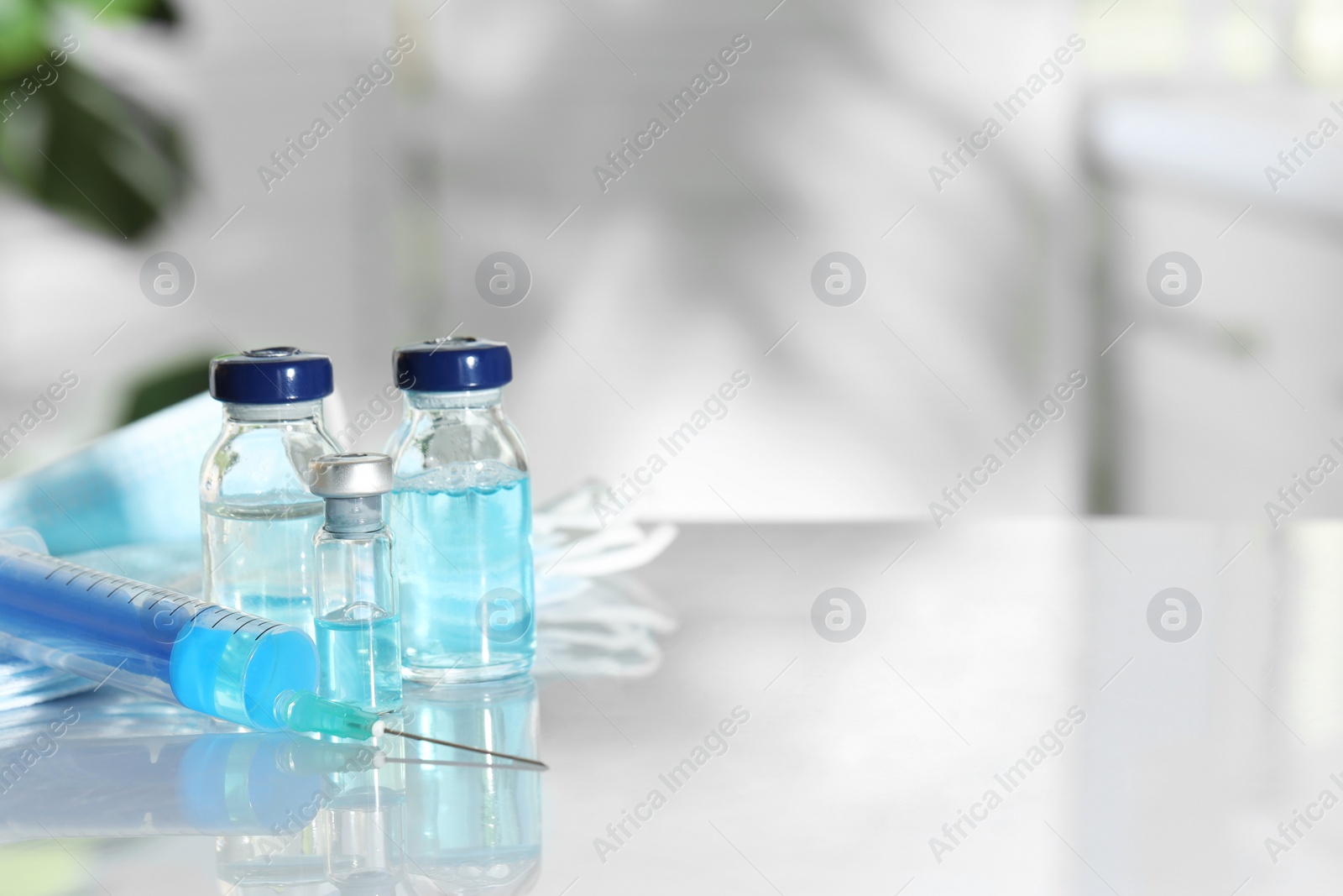 Photo of Glass vials, syringe and medical masks on white table. Space for text