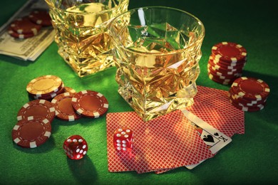 Photo of Casino chips, dice, playing cards and glasses of whiskey on green table