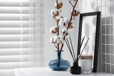 Reed diffuser, candle and cotton branches with fluffy flowers on white wooden table indoors. Space for text