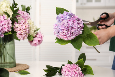 Woman pruning stem of hydrangea flower indoors, closeup. Interior design element