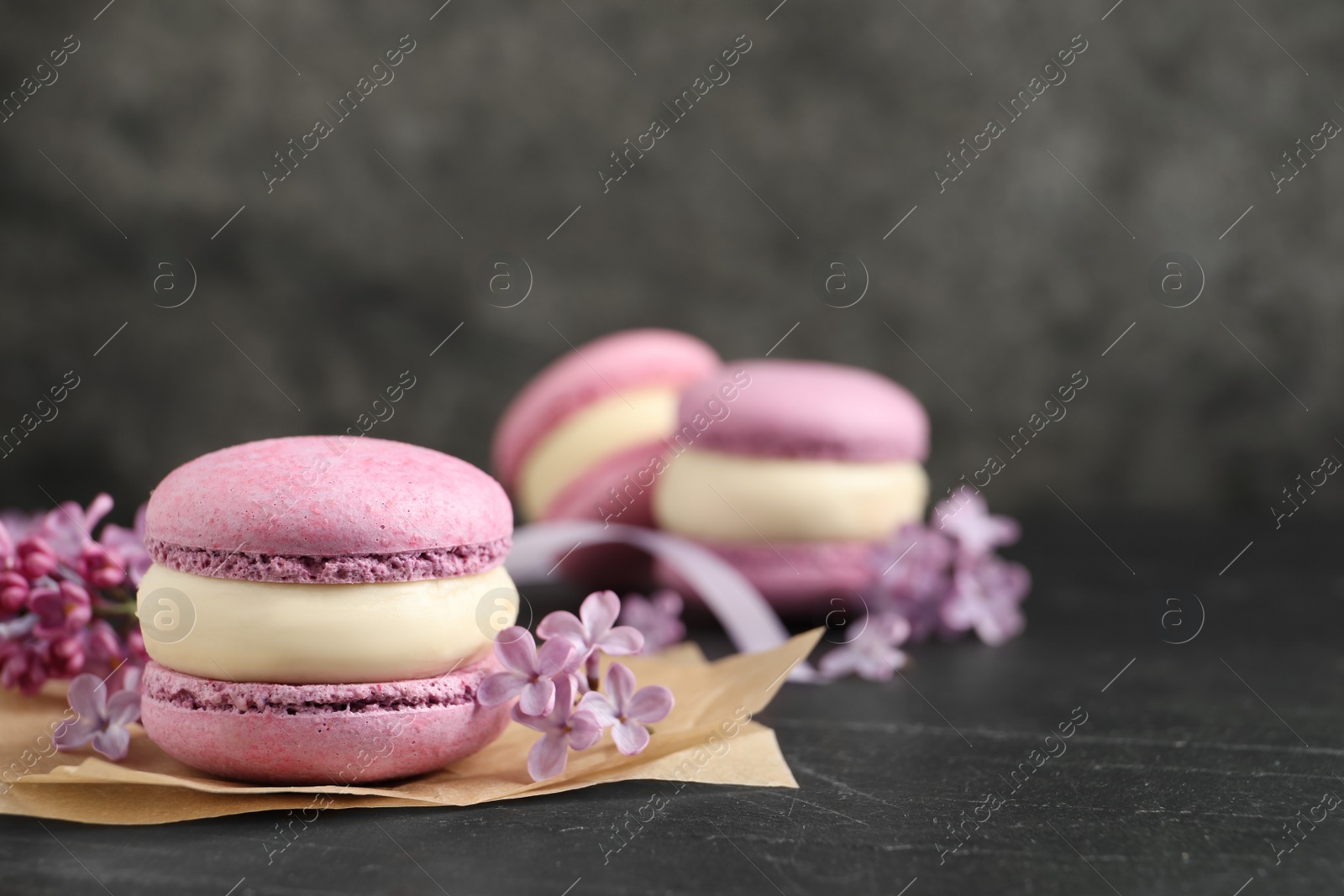 Photo of Delicious violet macaron and lilac flowers on black table, closeup. Space for text