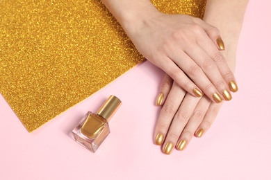 Woman showing manicured hands with golden nail polish on color background, closeup