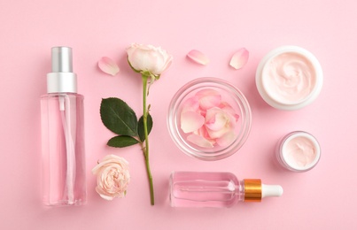 Flat lay composition with rose essential oil and flowers on pink background