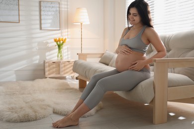 Photo of Pregnant young woman touching belly at home. Space for text
