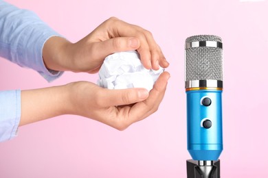 Photo of Woman making ASMR sounds with microphone and crumpled paper on pink background, closeup
