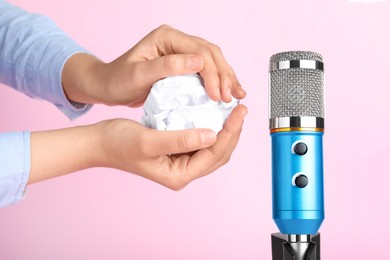 Woman making ASMR sounds with microphone and crumpled paper on pink background, closeup