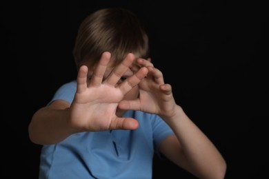 Boy making stop gesture against black background, focus on hands. Children's bullying