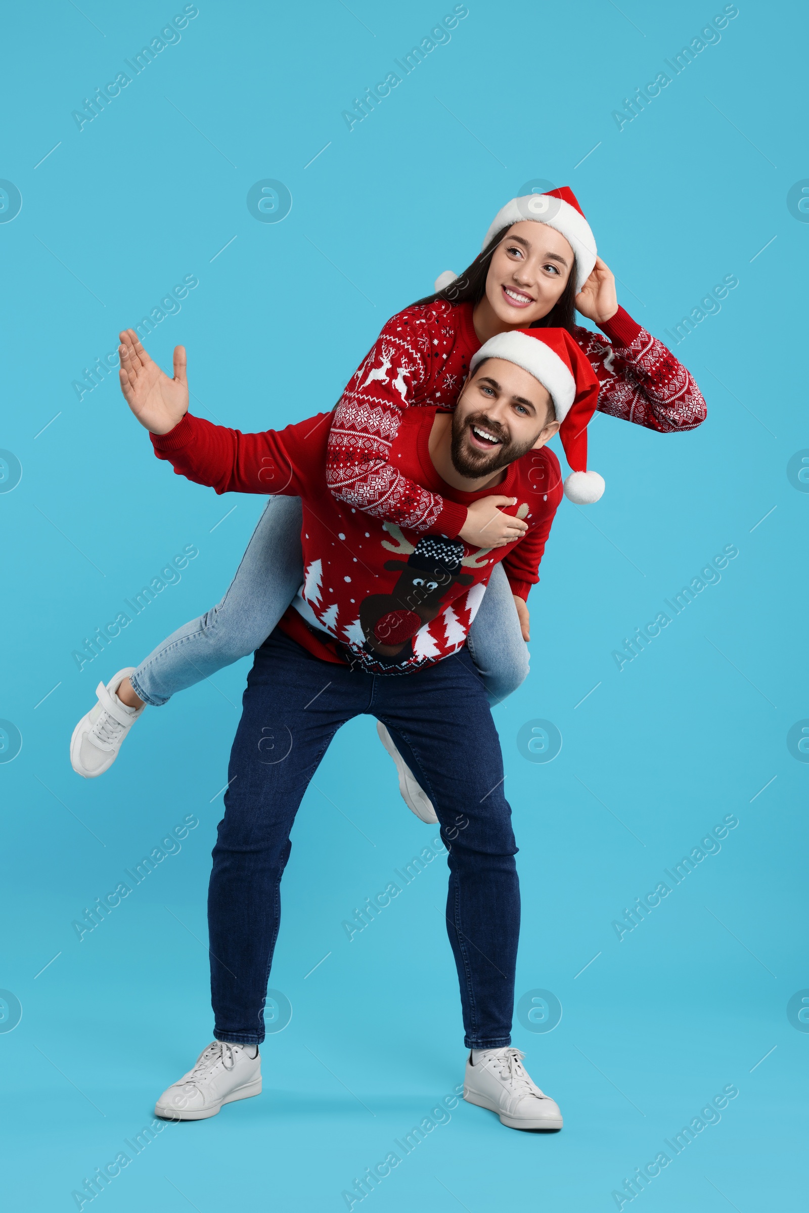 Photo of Happy young couple in Christmas sweaters and Santa hats on light blue background