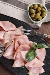 Tasty ham with basil, olives, peppercorns and carving fork on wooden table, flat lay