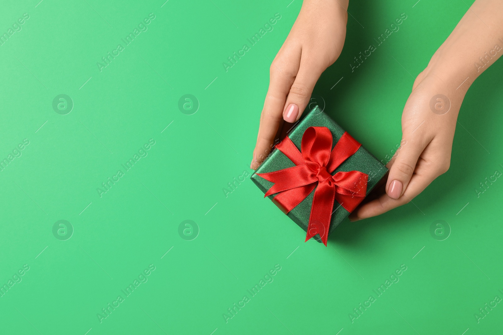 Photo of Woman with beautifully wrapped Christmas gift box on green background, top view. Space for text