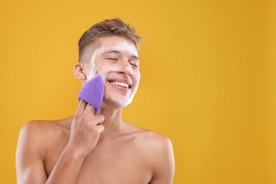 Photo of Happy young man washing his face with sponge on orange background. Space for text