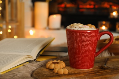 Photo of Cup of cocoa, books and cookies near fireplace indoors