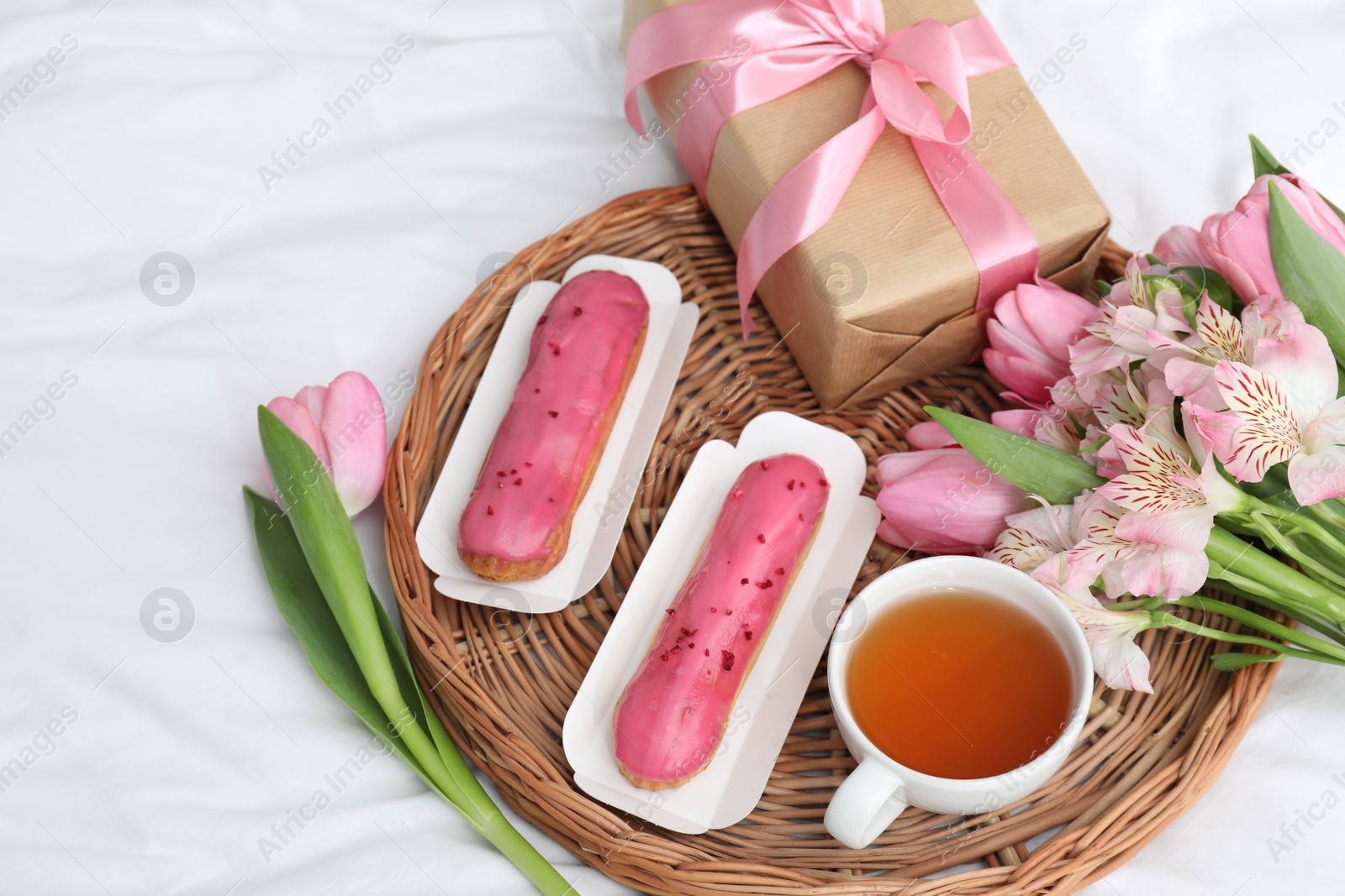 Photo of Tasty breakfast. Delicious eclairs, tea, flowers and gift box on bed