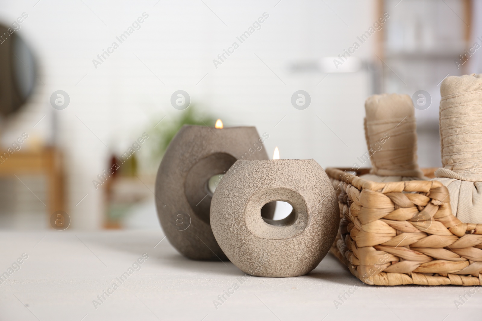 Photo of Burning candles and spa herbal bags on white table in bathroom, closeup. Space for text