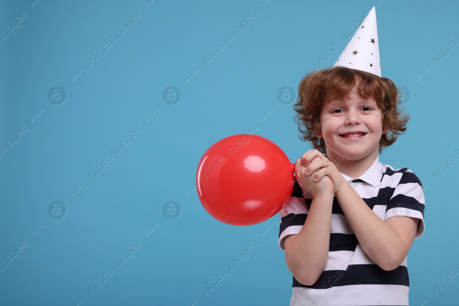 Photo of Happy little boy in party hat with balloon on light blue background. Space for text