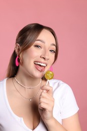Photo of Young woman with lip and ear piercings holding lollipop on pink background