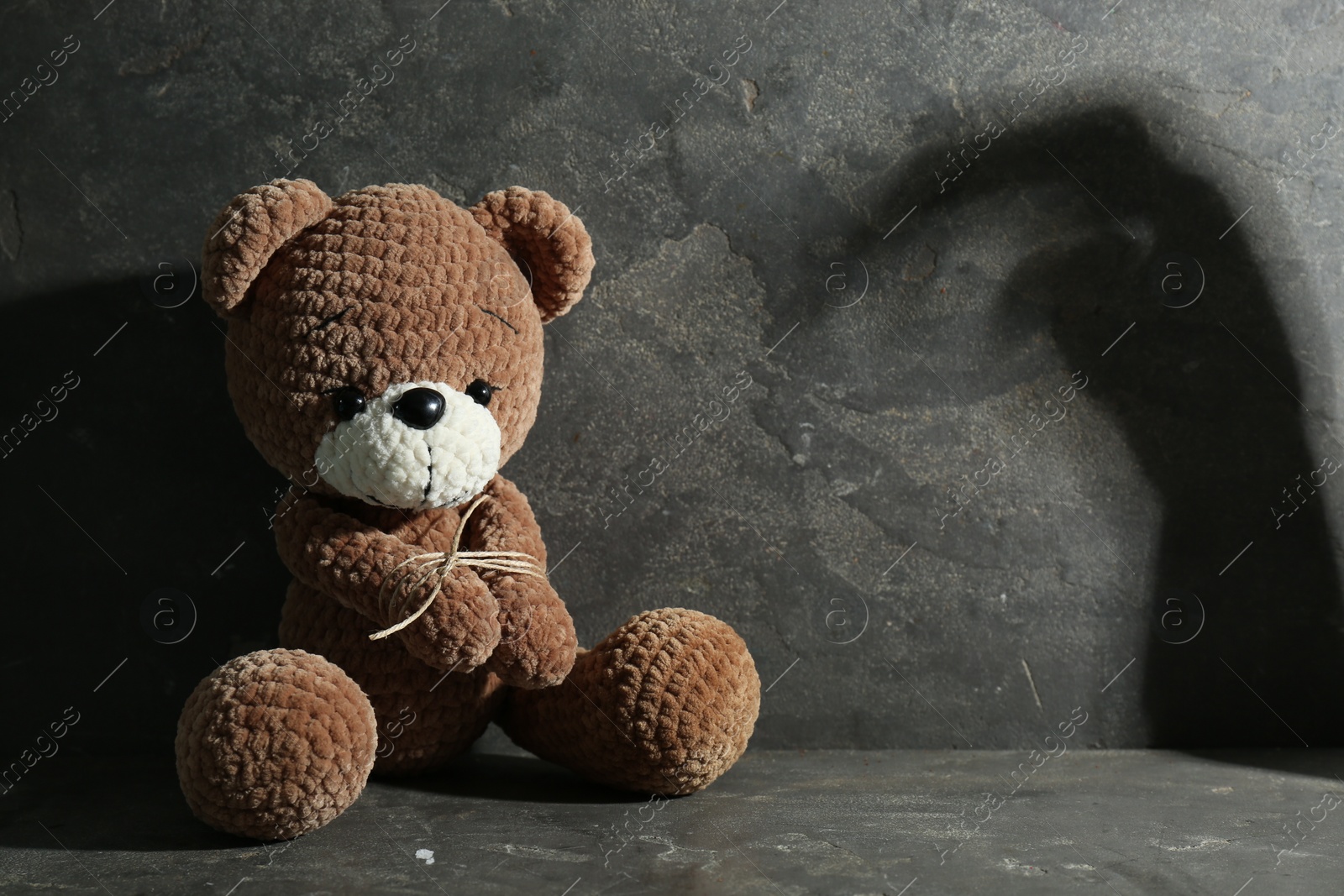 Photo of Stop child abuse. Tied toy bear and scary shadow in dark room